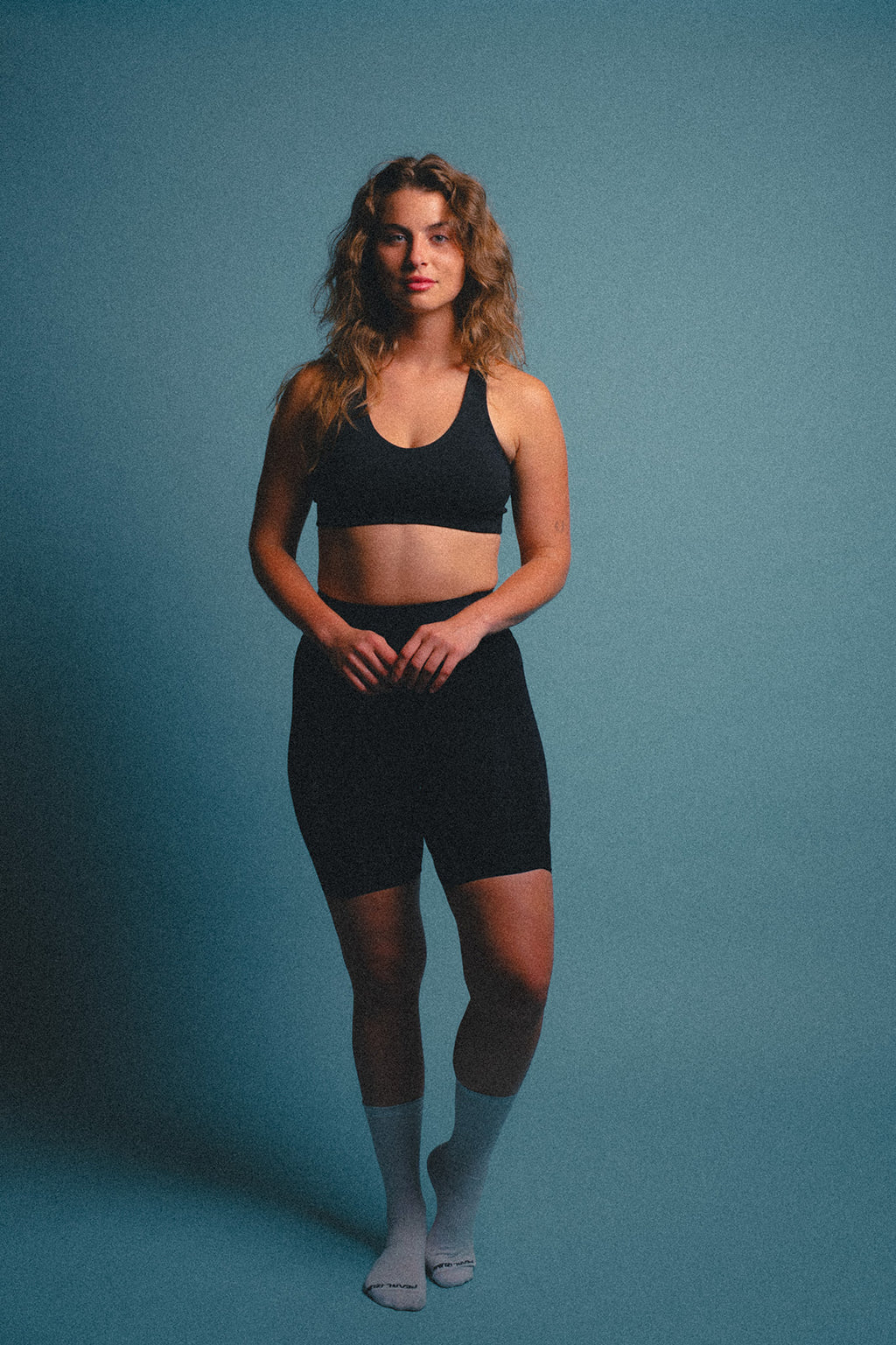 Woman wearing a black sports bra and cycling shorts on a blue background.