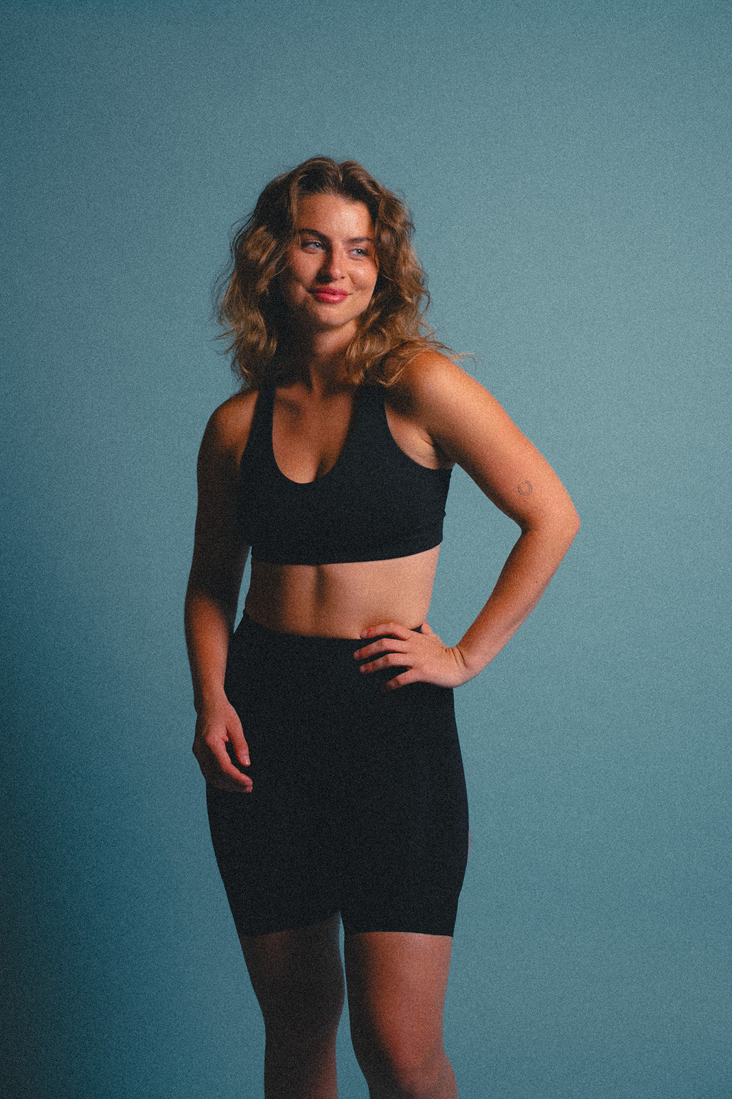 Woman wearing a black sports bra and cycling shorts against a blue background.