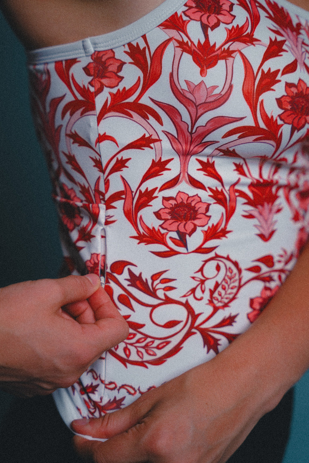 Woman wearing a red and white floral cycling jersey with a close-up of the fabric and hidden zippered key pocket.