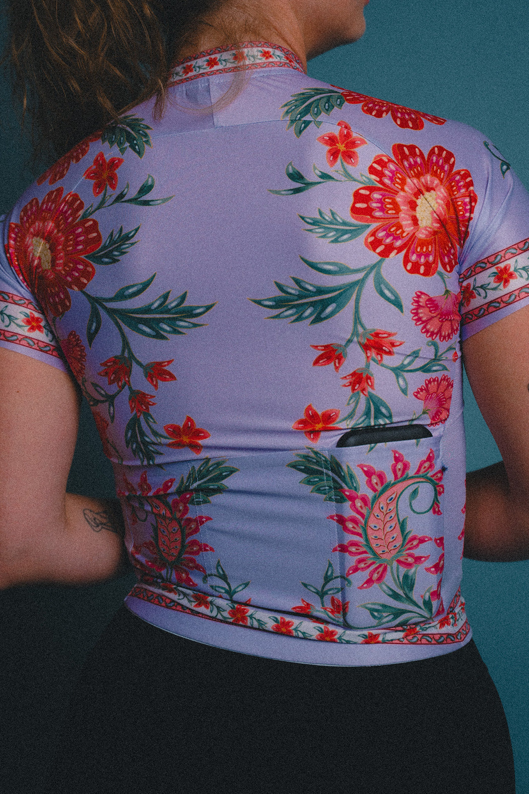 Floral patterned cycling jersey on a woman against a teal background