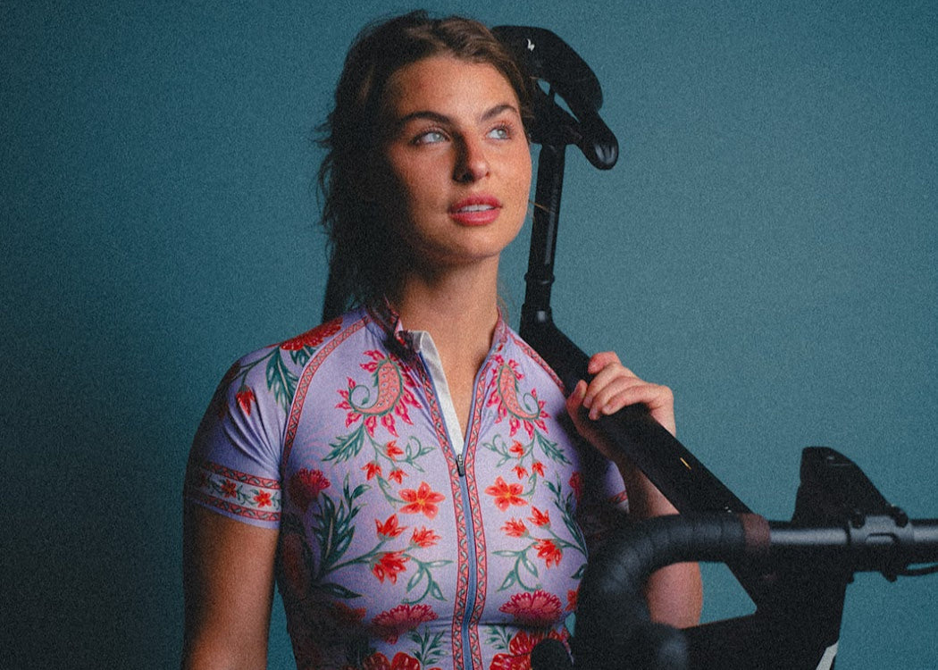 Woman wearing a colorful cycling jersey standing next to a bicycle against a blue background
